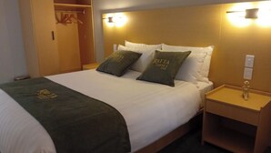 A hotel room with a bed, two pillows with the hotel name, a bedside table, and a wardrobe. - Rayya Suites, Paihia (Paihia)