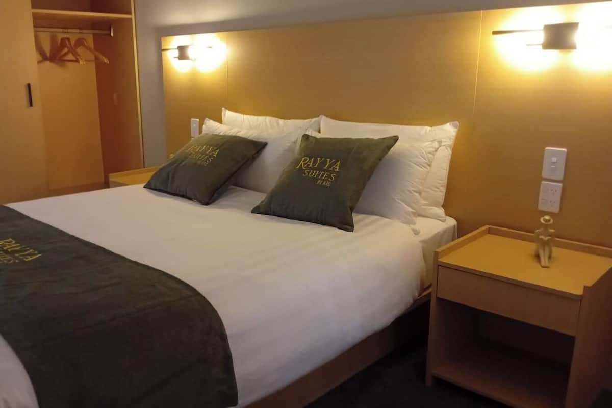 A hotel room with a bed, two pillows with the hotel name, a bedside table, and a wardrobe.