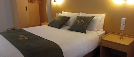 Ein Hotelzimmer mit einem Bett, zwei Kissen mit dem Hotelnamen, einem Nachttisch und einem Kleiderschrank.
