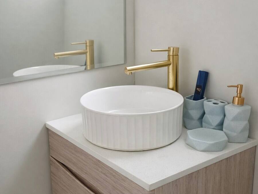 A bathroom with a white sink, gold faucets, and a mirror above it. There are toiletries on the counter.