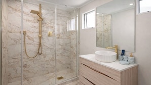 A modern bathroom with a glass-enclosed shower, marble walls, and a wooden vanity with a white sink. - Rayya Suites, Paihia (Paihia)