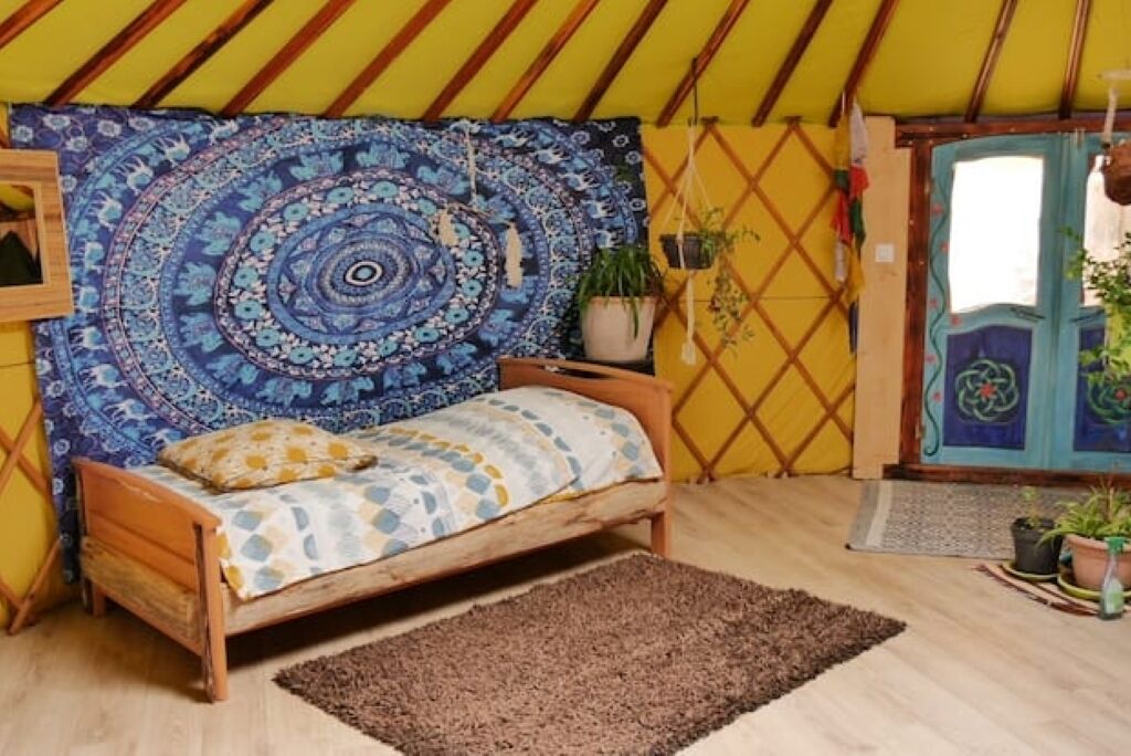 A cozy room with a wooden bed, a blue patterned tapestry, and a wooden door.