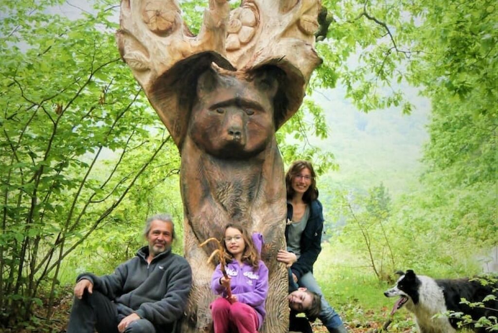 A group of people sitting and posing around a large tree sculpture with a carved face.