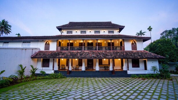 Un edificio de estilo colonial de dos pisos con techo de tejas, un balcón en el nivel superior y un porche delantero cubierto con asientos.