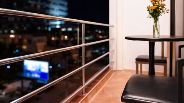 A balcony with a metal railing, a small round table with a vase of flowers, and a black leather chair. - Baan Kamala Backpacker (Kamala)