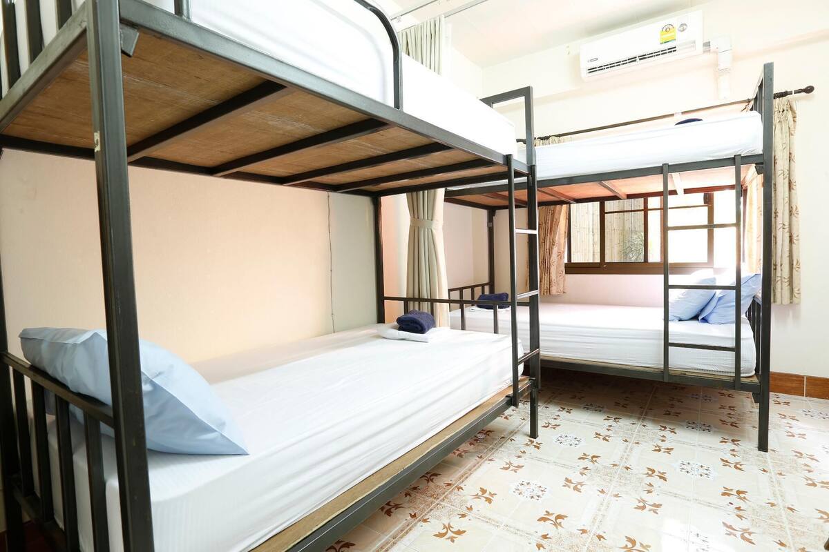 A bunk bed room with a window, curtains, and an air conditioning unit.