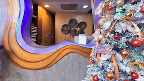 A reception area with a curved wooden reception desk, a Christmas tree decorated with ornaments, and a wall with circular decorations. - Baan Kamala Backpacker (Kamala)