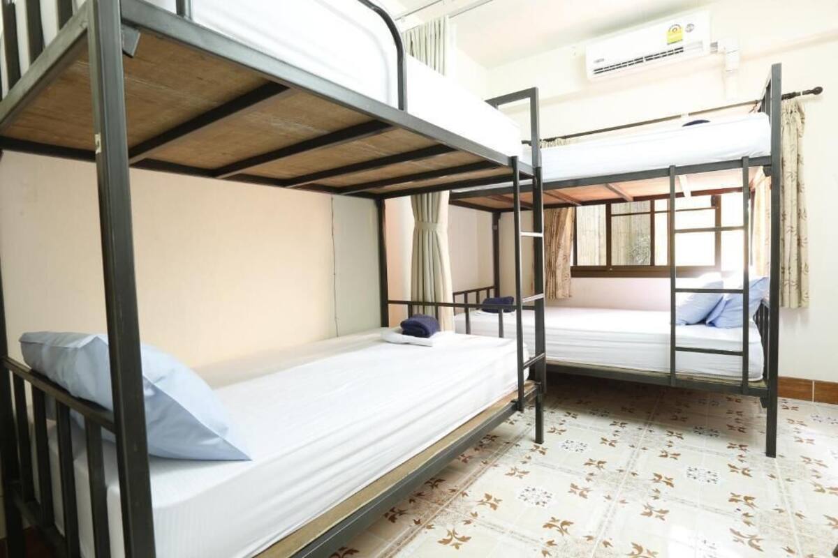 A dormitory room with bunk beds, a window with curtains, and a patterned floor.