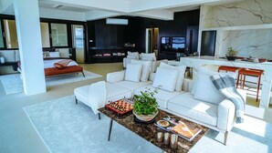 A modern living room with a white sofa, a coffee table with a chess set and a plant, and a TV in the background.