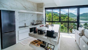 A modern kitchen with a black refrigerator, marble backsplash, and a large window overlooking a scenic landscape.