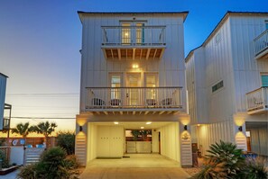 Un edificio a due piani con un balcone al piano superiore, un accesso al garage e un vialetto recintato.