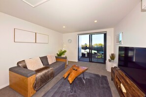 A modern living room with a sofa, a coffee table, a TV, and a sliding glass door leading to an outdoor area. - Fresh 1BR City Base on Manchester (Christchurch)