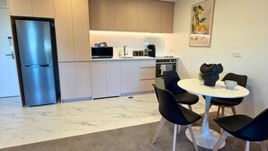 Una cocina moderna con refrigerador, microondas y estufa incorporados. Hay una zona de comedor con una mesa redonda y cuatro sillas.