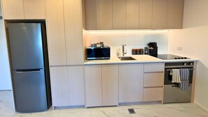 Una cocina moderna con armarios de madera clara, un refrigerador de acero inoxidable, un microondas, un lavamanos y un horno.