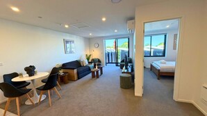 Una sala de estar moderna con sofá, mesa de centro y sillones, un comedor con mesa y sillas, y un dormitorio con cama y ventana.