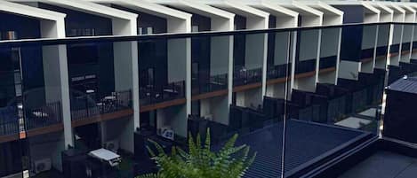 Un edificio moderno con fachada de vidrio y una terraza en la azotea con planta en maceta.