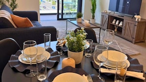 A dining area with a table set for two, a sofa, a TV, and a balcony view. - Minimalist City Stay – Manchester Street (Christchurch)