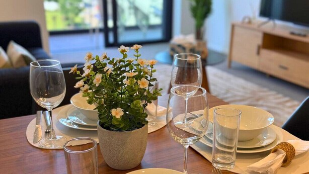 A dining table set with white plates, bowls, and cutlery, a small potted plant, and clear glasses. - Fresh Build City Retreat in Christchurch CBD (Christchurch)