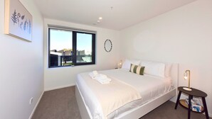 A bedroom with a large bed, a small bedside table, a window with a view, and a wall-mounted light fixture. - Fresh Build City Retreat in Christchurch CBD (Christchurch)