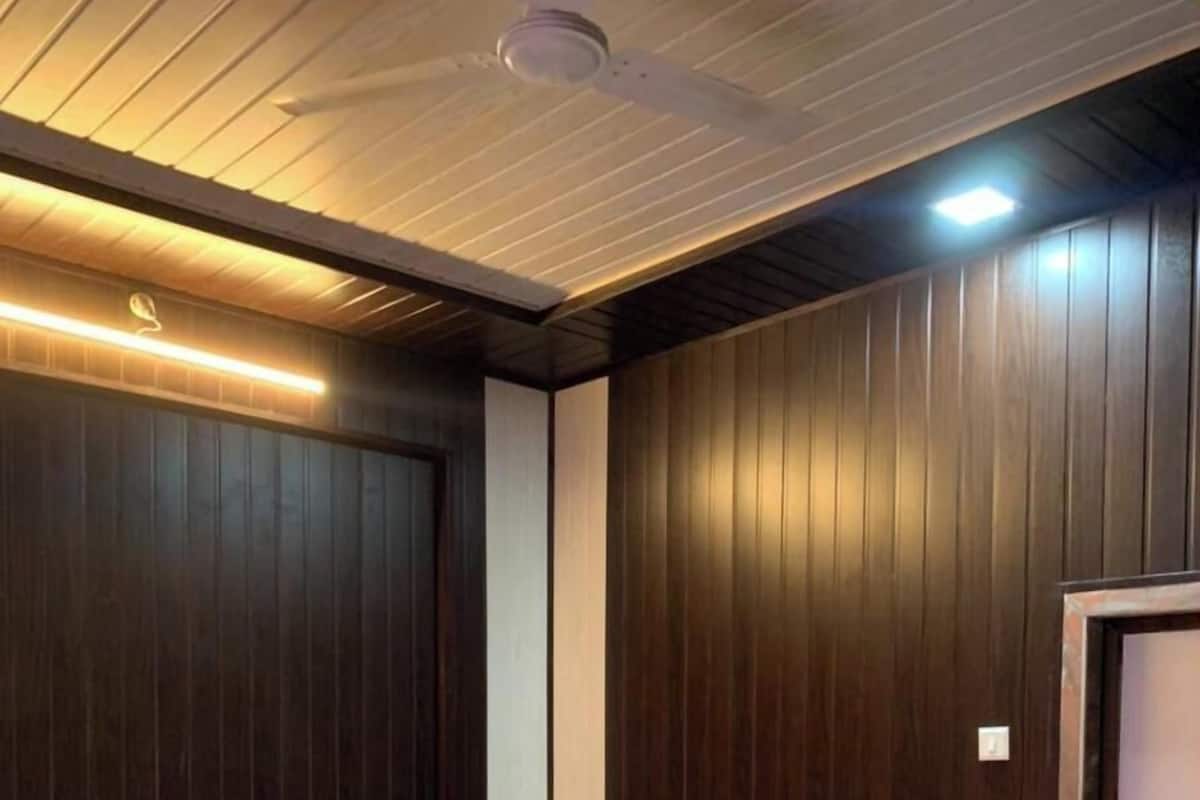 Ein Hotelzimmer mit einem großen Bett, zwei rot und schwarz gepolsterten Sesseln, einer Wand aus Holzpaneelen und einem Deckenventilator.