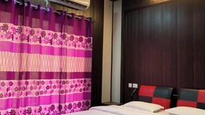 Ein Hotelzimmer mit Bett, Deckenventilator, Klimaanlage und einem Fenster mit violetten Vorhängen.