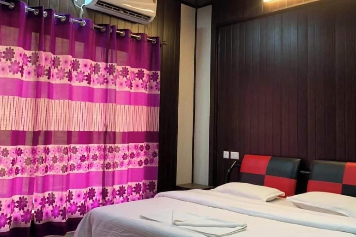 Ein Hotelzimmer mit Bett, Deckenventilator, Klimaanlage und einem Fenster mit violetten Vorhängen.