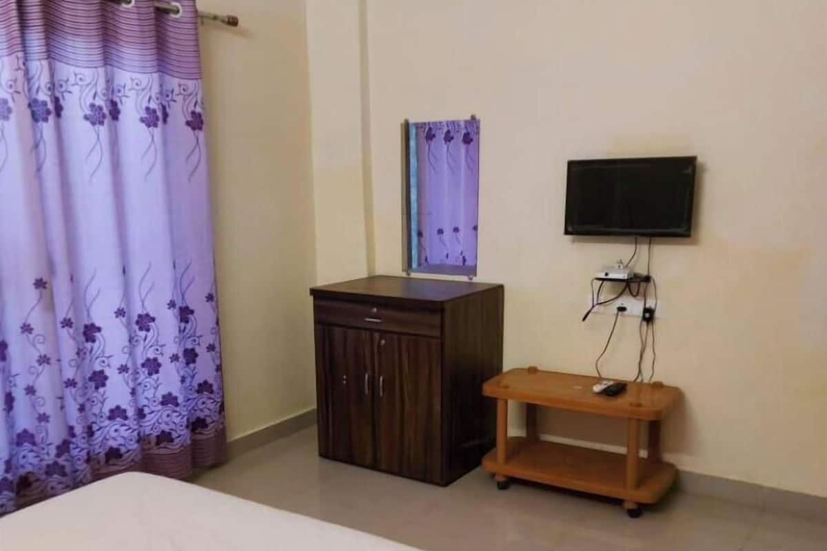 Ein Schlafzimmer mit einem Bett, einem Holzkasten, einem an der Wand befestigten Fernseher und einem Vorhang mit floralem Muster.