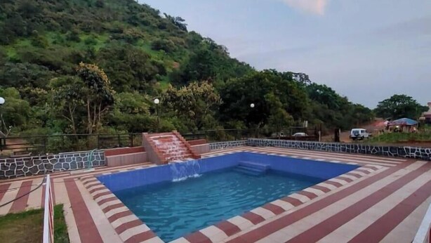Ein Schwimmbecken mit rotem und weißem Fliesensaum, umgeben von einer Steinmauer und einer Rasenfläche.