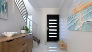 A modern hallway with a wooden console, a black door with illuminated panels, a staircase, and a painting of a seascape.