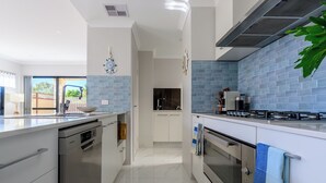 A modern kitchen with white cabinetry, a blue backsplash, stainless steel appliances, and a view of the outdoors.