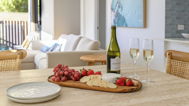 A dining table with a bottle of Edenvale sparkling wine, two glasses, a wooden board with grapes, strawberries, and crackers, and a white plate.