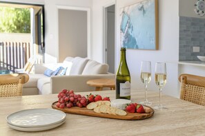 Une table à manger avec une bouteille de vin mousseux Edenvale, deux verres, une planche en bois avec des raisins, des fraises et des crackers, et une assiette blanche.