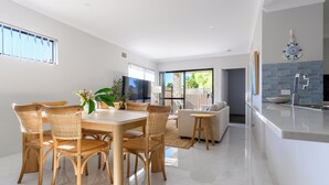 A modern kitchen with a large island, a dining area with wicker chairs, and a living area with a sofa.
