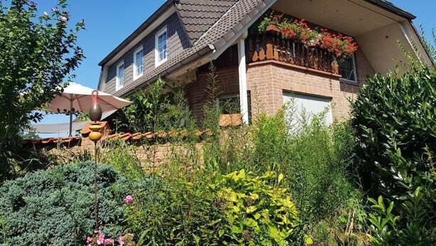 Une maison à deux étages, avec un toit en pente, une façade en briques et un balcon orné de fleurs rouges.