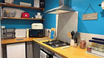 A compact kitchen with a microwave, gas stove, and a small refrigerator.
