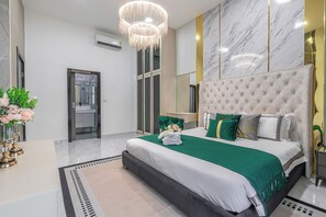 Ein modernes Schlafzimmer mit einem großen Bett, einer Kristallleuchter, einem Spiegel und Blick ins Badezimmer.