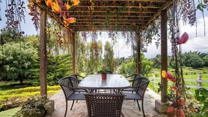 A covered outdoor dining area with a round table and four chairs, surrounded by stone flooring and lush greenery. - El Oasis Organic Farm (Piedecuesta)