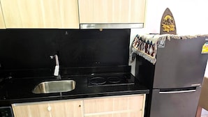 A kitchen with a black countertop, stainless steel sink, and a refrigerator. - Budget Studio Condo with Resort-Style Pool - Laguna Beach Resort 1, Jomtien (Muang Pattaya)