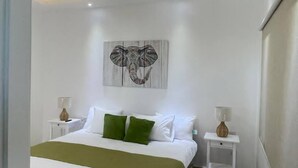 A modern bedroom with a large bed, a ceiling light, a wall-mounted artwork, and bedside tables. - Luxurious 3-Bedroom Apartment in Juan Dolio with Pool Access (Juan Dolio)