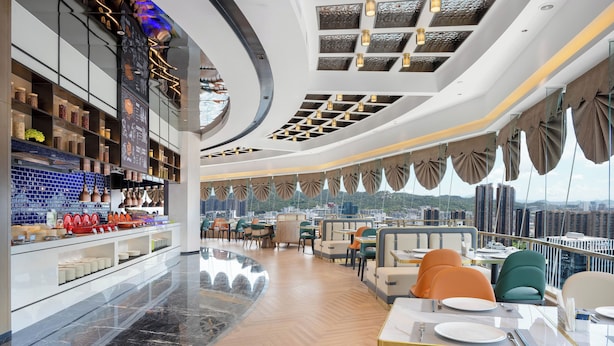 A modern restaurant with a high ceiling, glass railings, and a city view. - Hampton by Hilton  Hubin South Road (Xiamen)