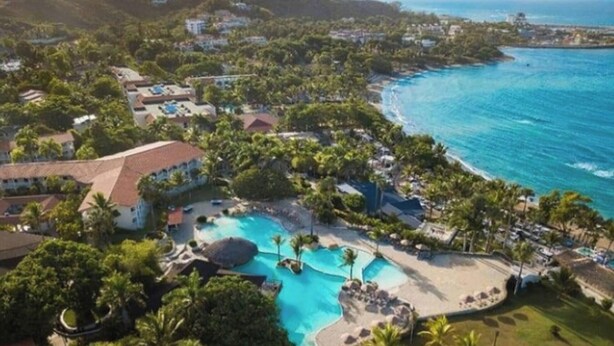 Et resort med en stor pool, palmer og havudsigt.