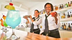 En bar med bartendere, der laver drinks, og et udvalg af spiritusflasker i hylderne.