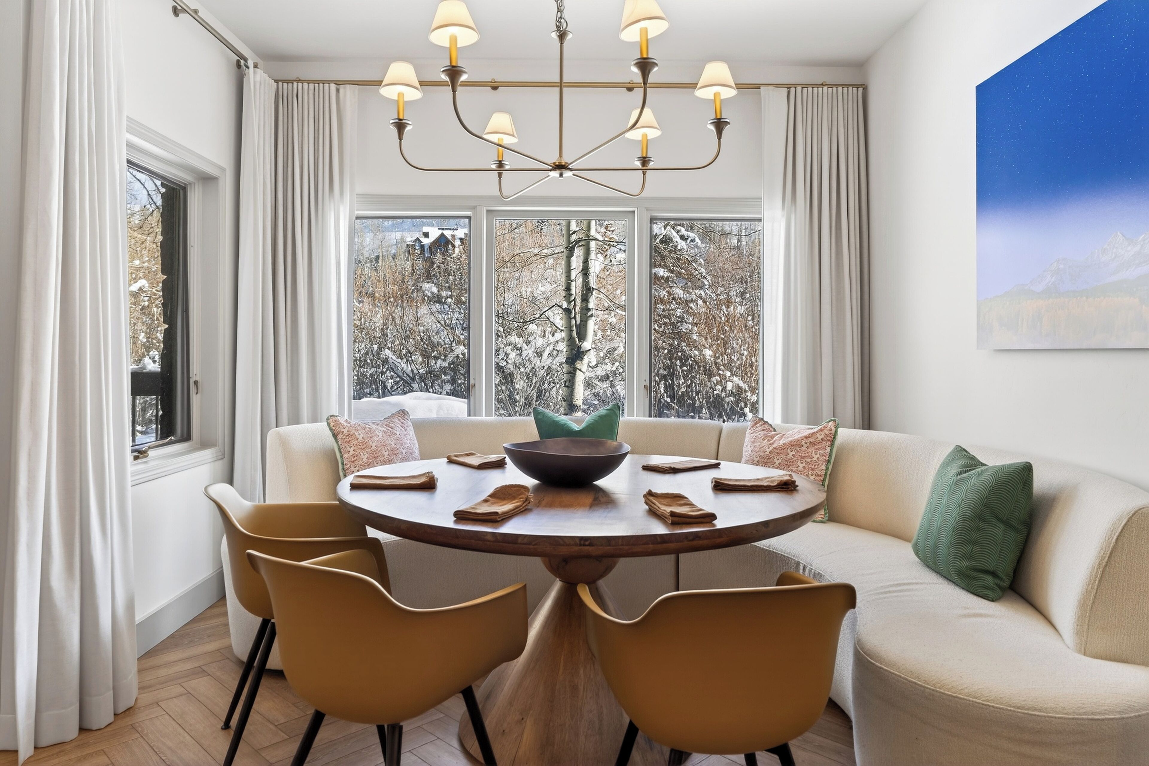 Un coin repas comprenant une table ronde, des chaises, un lustre et un canapé avec des coussins.