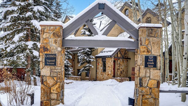 Entrada coberta de neve, com pilares de pedra e estrutura de telhado metálico.