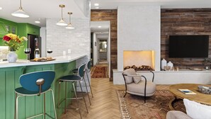 Uma cozinha moderna com armários verdes, um espaço de bar com banquetas, lareira e uma televisão de tela plana na parede.
