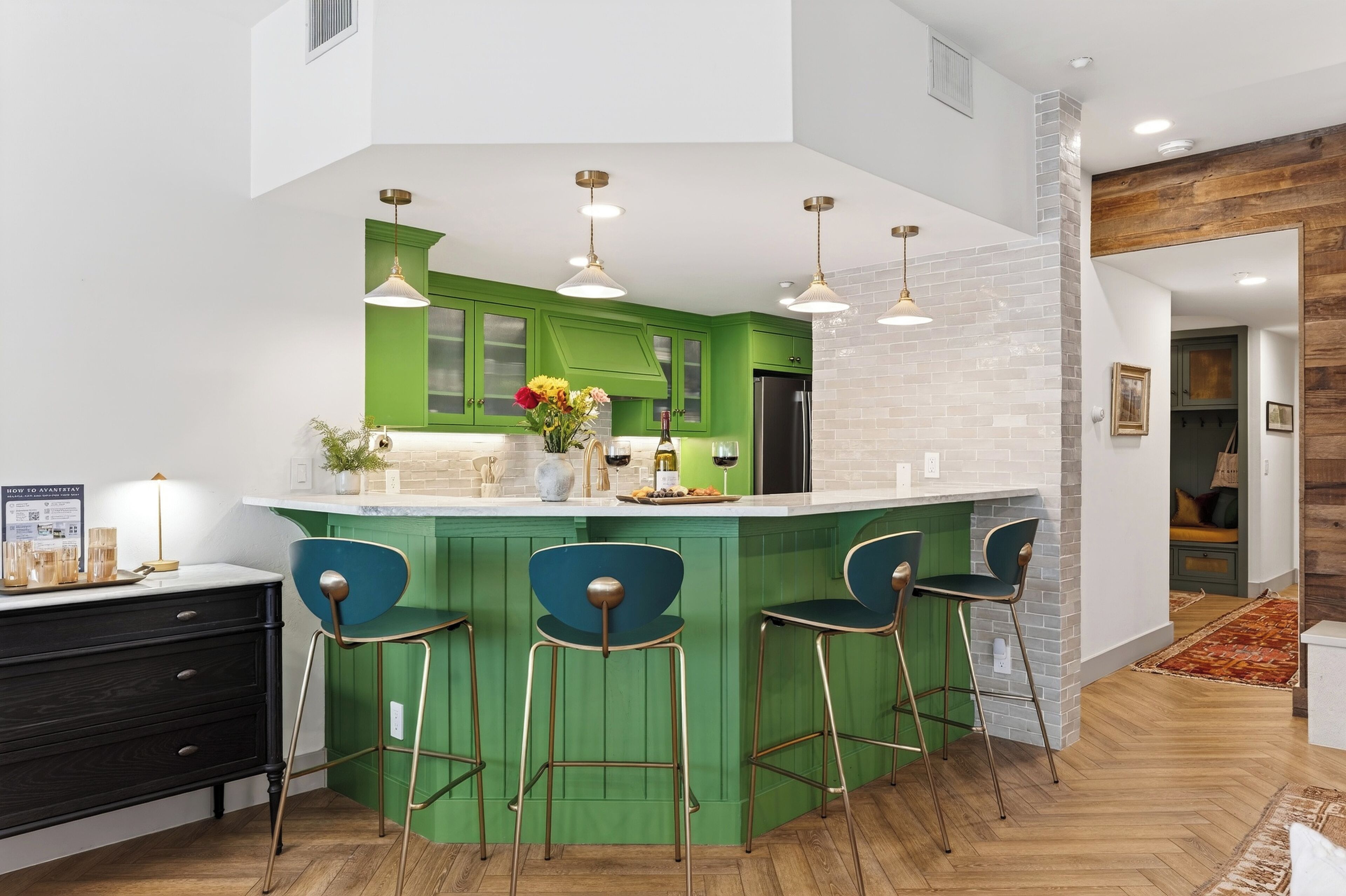 Une cuisine moderne avec des meubles de couleur verte, un îlot central doté de tabourets de bar, un éclairage suspendu et une vue sur le salon attenant.