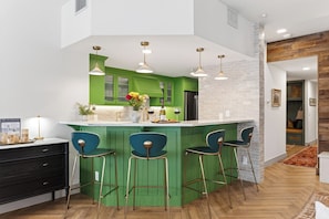 A modern kitchen with green cabinets, a central island with bar stools, pendant lighting, and a view into the adjacent living area. - Slopeside Mountain Village Home + Hot Tub Access + Near Lift, Gondola & Dining (Mountain Village)