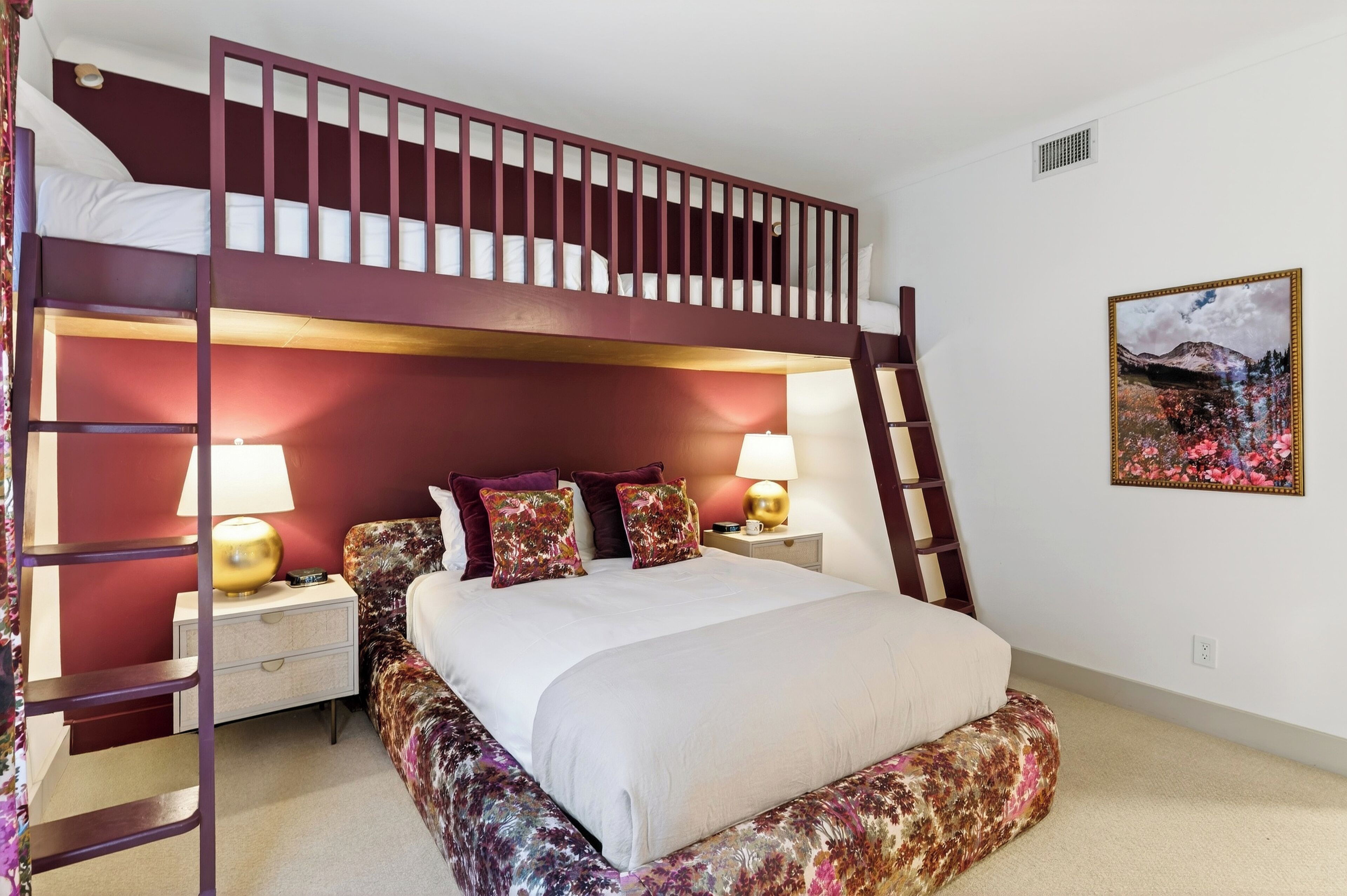 Una cama litera con escalera de madera, dos mesitas de noche con lámparas y una falda de cama estampada con motivos florales.