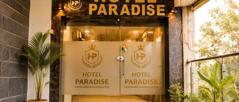 The entrance of Hotel Paradise with a clear view of the reception area, including the hotel's name and logo on the glass doors.