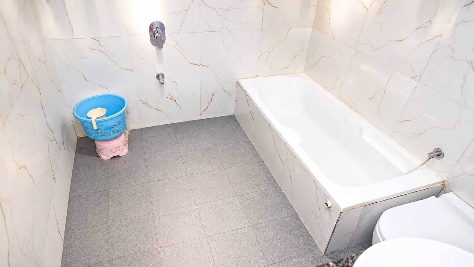 A bathroom with a bathtub, toilet, and a blue bucket.